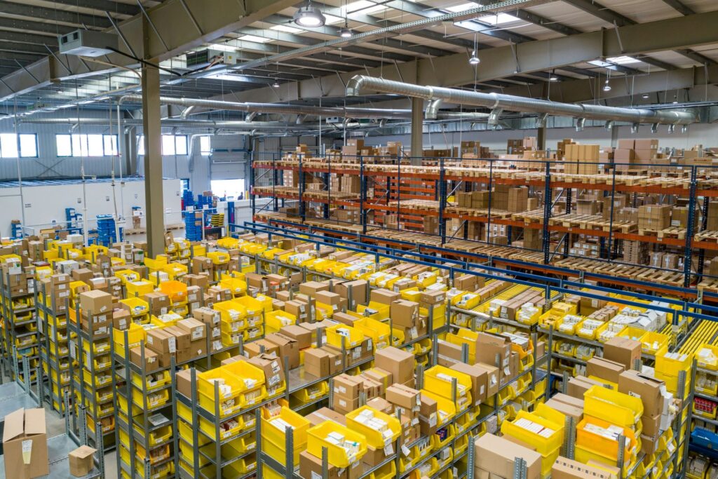 adriansulyoksczNLg6rrhQunsplash | Resource Tool for Startup and Small Businesses in New Mexico Interior of a large warehouse with tall racks yellow plastic bins and numerous cardboard boxes lined up on shelves