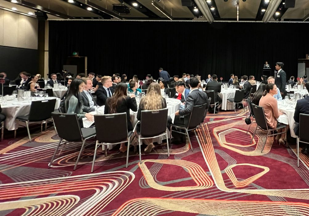 Crowd of formally dressed people seated at round tables in a large banquet hall likely a conference dinner