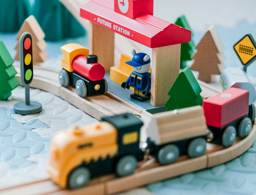 train set | Resource Tool for Startup and Small Businesses in New Mexico Wooden toy train set on a curved track with a red station signal trees and a blue figure beside the platform